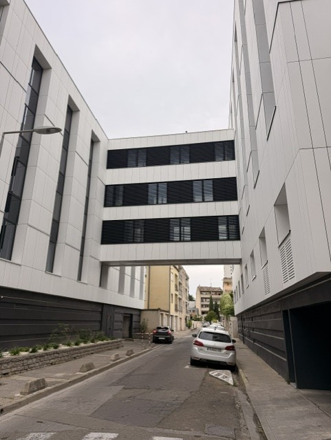 Passerelle entre bâtiments revêtue de panneaux fibres-ciment et bandeaux de ventilation noirs